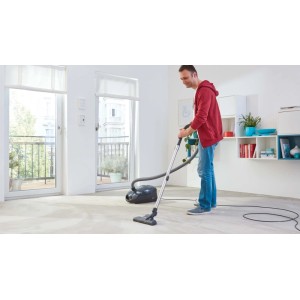 Mężczyzna odkurza dywan w salonie za pomocą odkurzacza.