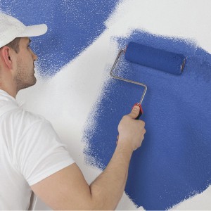 Mężczyzna maluje ścianę niebieskim wałkiem. Kategoria: Wałki malarskie.
