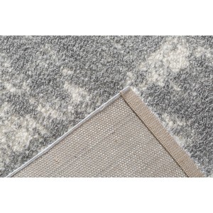 Szaro-biały dywan z długim włosiem, zbliżenie na róg i spód.