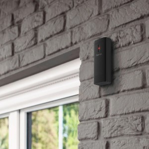 Czarny czujnik stacji pogodowej zamontowany na szarej ceglanej ścianie.