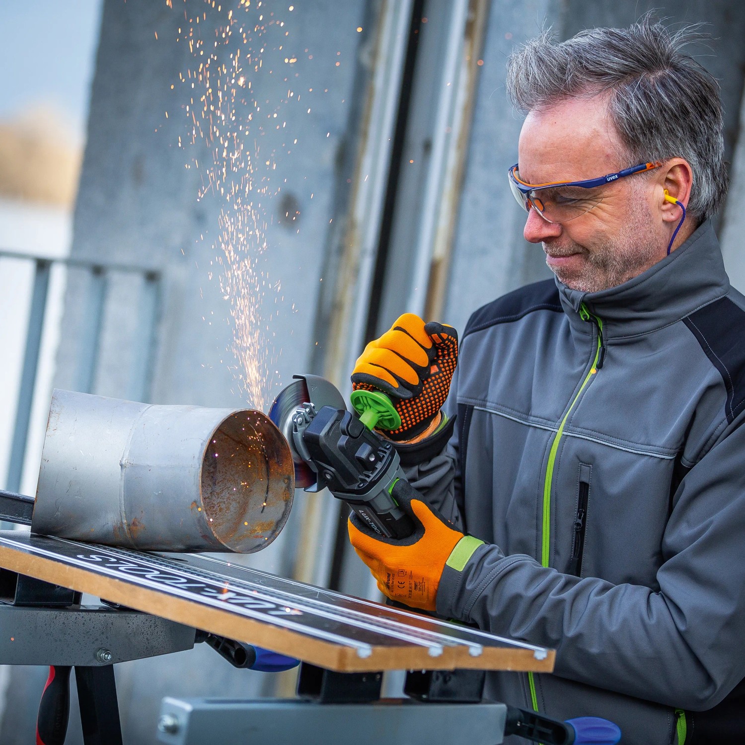 Mężczyzna szlifuje metalową rurę akumulatorową szlifierką kątową LUX A-WS-20/115. Lecą iskry.
