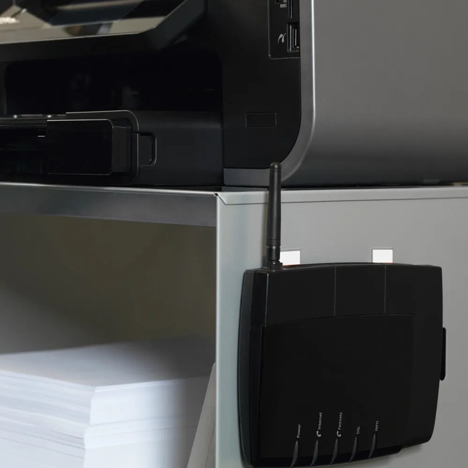Czarny router z anteną, przymocowany taśmą t.b.t. pod drukarką.
