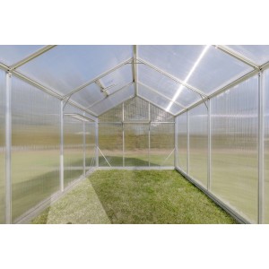 Wnętrze szklarni z przezroczystymi ścianami i trawiastą podłogą.