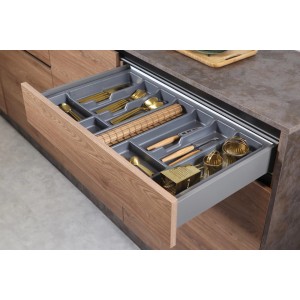 Otwarta szuflada kuchenna z szarym wkładem na sztućce i złotymi sztućcami.