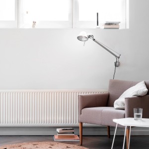 Salon z szarobrązowym fotelem, grzejnikiem, lampą ścienną i białą farbą do ścian.