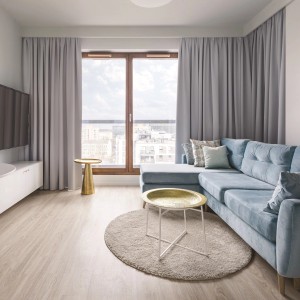 Salon z szarymi zasłonami, niebieską sofą i jasnym dywanem.