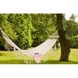 Biały hamak rozpięty między drzewami w ogrodzie. Czysty relaks z odpowiednią huśtawką ogrodową.