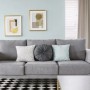 Szara sofa z poduszkami przed ścianą z abstrakcyjnymi obrazami. Kolorowe farby do ścian.