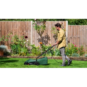 Mężczyzna obsługuje zieloną kosiarkę elektryczną t.b.t. w ogrodzie.
