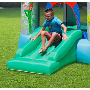 Chłopiec zjeżdża na zielonej zjeżdżalni na dmuchanym placu zabaw.