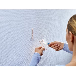 Kobieta przykleja samoprzylepny haczyk t.b.t. do ściany. Praktyczne rozwiązanie bez wiercenia.