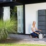 Szary zbiornik na deszczówkę 4rain Slim Stone Decor 330 l z kobietą i konewką przed ścianą domu.