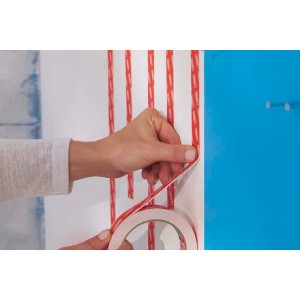 Naklejanie taśmy klejącej t.b.t. na ścianę. Widoczne: rolka taśmy i ręka.