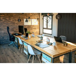 Biuro z długim drewnianym stołem, krzesłami i komputerami na tle ceglanej ściany.
