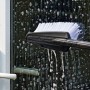 Ręka czyści okno szczotką myjącą Bosch do myjki ciśnieniowej. Czarna szczotka z białym włosiem, woda z mydłem.