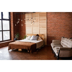 Przytulna sypialnia z ceglaną ścianą i drewnianym łóżkiem. Elementy dekoracyjne w pokoju.