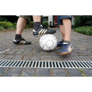 Zdjęcie kanału odwadniającego t.b.t. z bawiącymi się dziećmi i piłką nożną w ogrodzie.