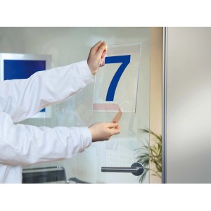 Osoba przykleja niebieską cyfrę 7 do szklanych drzwi za pomocą taśmy t.b.t.