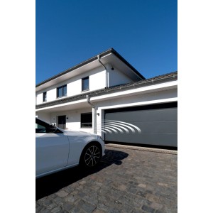 Nowoczesny dom z szarą bramą garażową t.b.t. i białym samochodem przed nim.