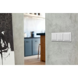 Białe ramki t.b.t. do włączników i gniazdek na szarej ścianie.