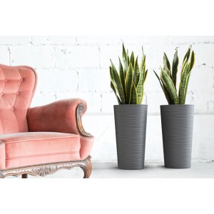 Grafitowa doniczka Lilia Dluto, 30x57cm, z żebrowaną powierzchnią obok fotela.