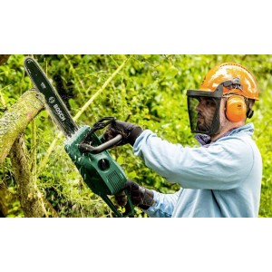 Mężczyzna w kasku ochronnym i z piłą łańcuchową tnie drzewo. Piła łańcuchowa w użyciu.