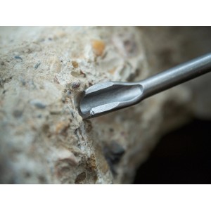Zbliżenie dłuta kanałowego LUX SDS Plus (22x250mm) w użyciu na ścianie betonowej.
