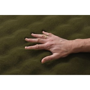 Dłoń wciska się w miękki, oliwkowozielony dywan z długim włosiem.