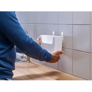 Mężczyzna mocuje biały, samoprzylepny wieszak t.b.t. do ściany z płytek w łazience lub kuchni.