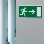 Zielony znak wyjścia ewakuacyjnego z białym piktogramem biegnącej osoby i strzałką.