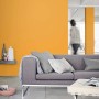 Salon z żółtą farbą na ścianach, szara sofa z poduszkami. Kolorowa farba do ścian wewnętrznych.