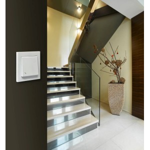 Biały włącznik światła t.b.t. na ciemnej ścianie na klatce schodowej.