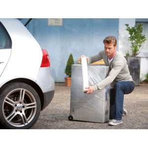 Mężczyzna owija walizkę folią stretch LUX (0,5 m x 120 m) przed samochodem. Materiał osłonowy do przeprowadzki.