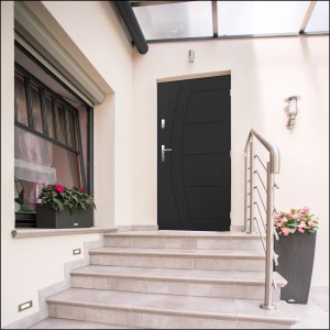 Nowoczesne szare drzwi wejściowe z klamką ze stali nierdzewnej przed jasnym wejściem.