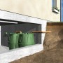Zielona cysterna Garantia Herkules 1600 l w przekroju z ziemią i ścianą domu.