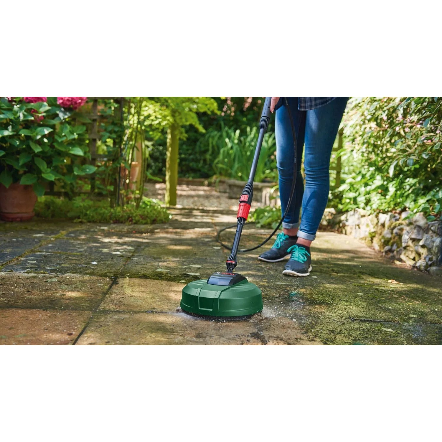 Osoba czyści taras myjką ciśnieniową Bosch Universal Aquatak 125 i zielonym środkiem do czyszczenia powierzchni. Czyste płyty.
