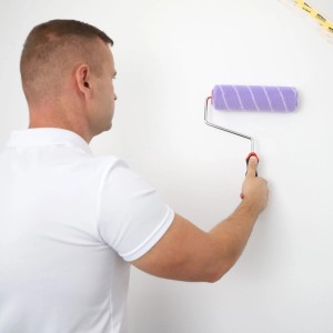 Mężczyzna maluje ścianę fioletowym wałkiem t.b.t.