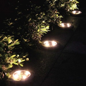 Rząd okrągłych lamp solarnych t.b.t. wzdłuż ciemnej ścieżki ogrodowej.